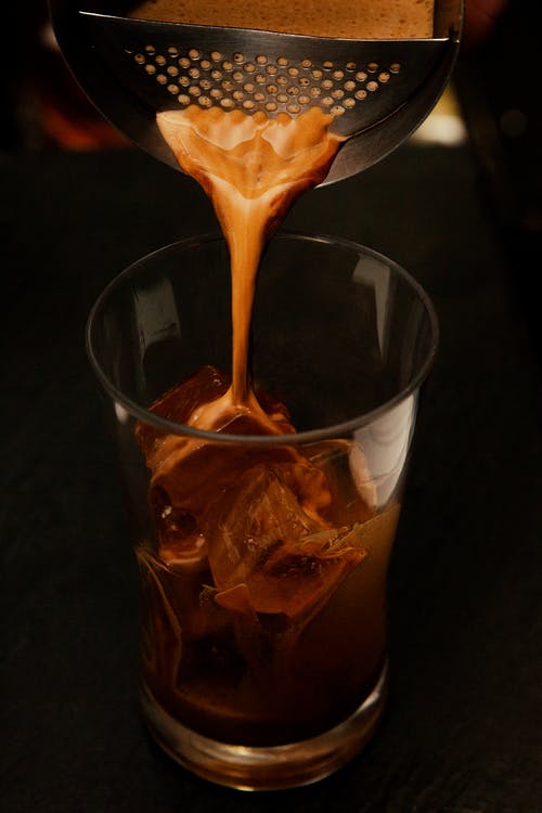 coffee being poured through strainer into glass with ice cubes