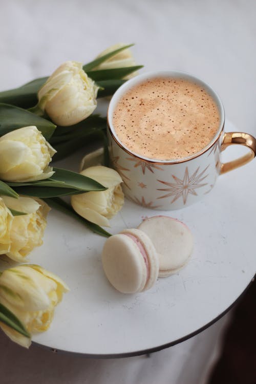 latte in ceramic cup with macarons and white roses