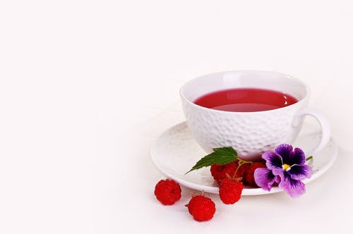 raspberry tea in white cup with raspberries and purple flowers